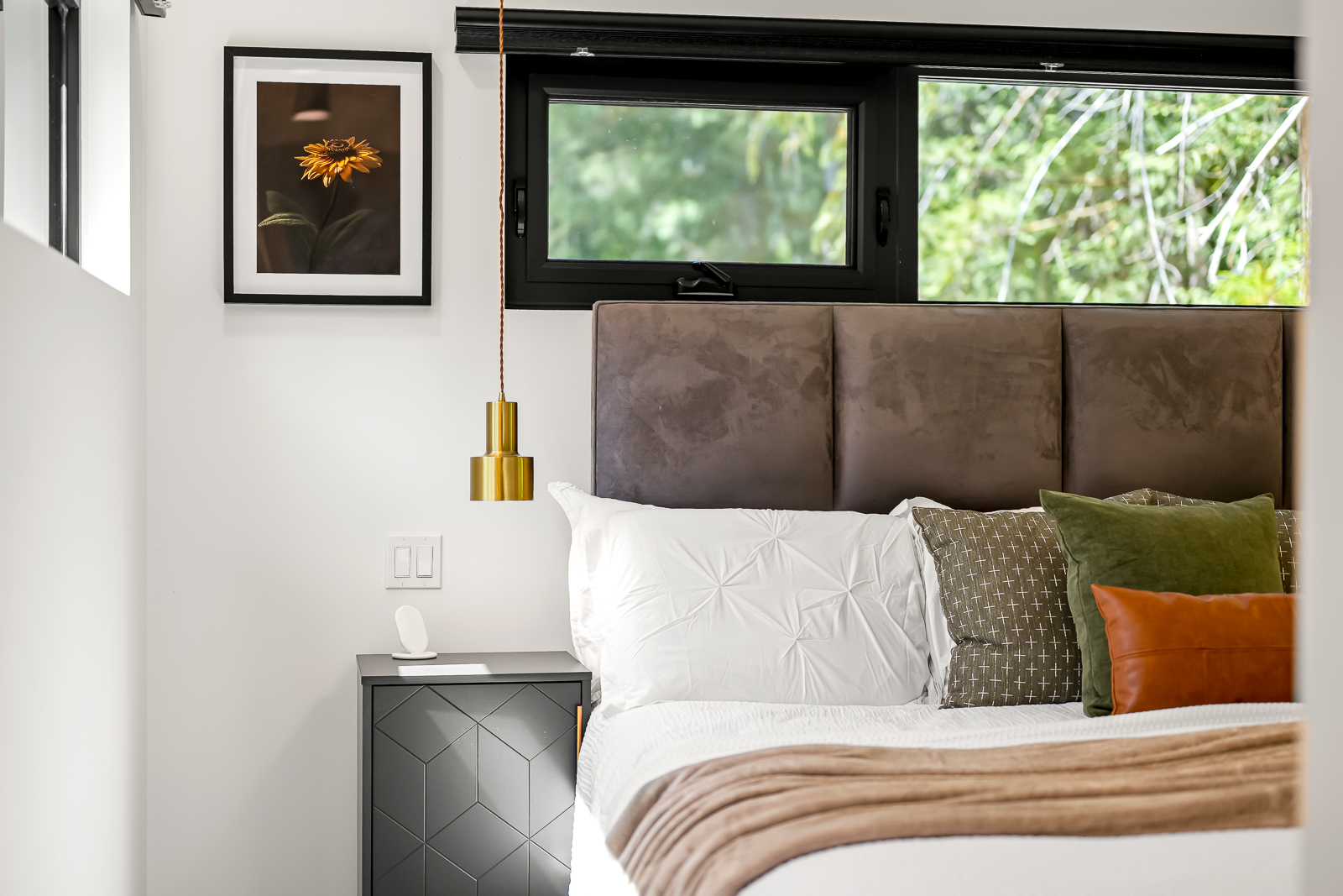 Primary bedroom with velvet headboard, brass pendant, and forest light