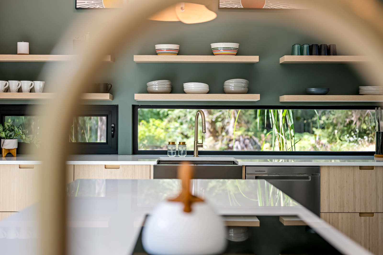 Kitchen detail — the forest-view window backsplash framed through the brass faucet