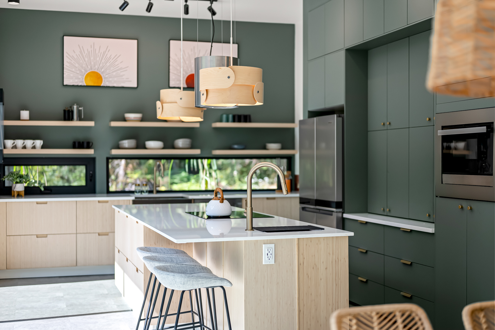 The kitchen with waterfall stone island, sage green cabinets, and forest-view window backsplash
